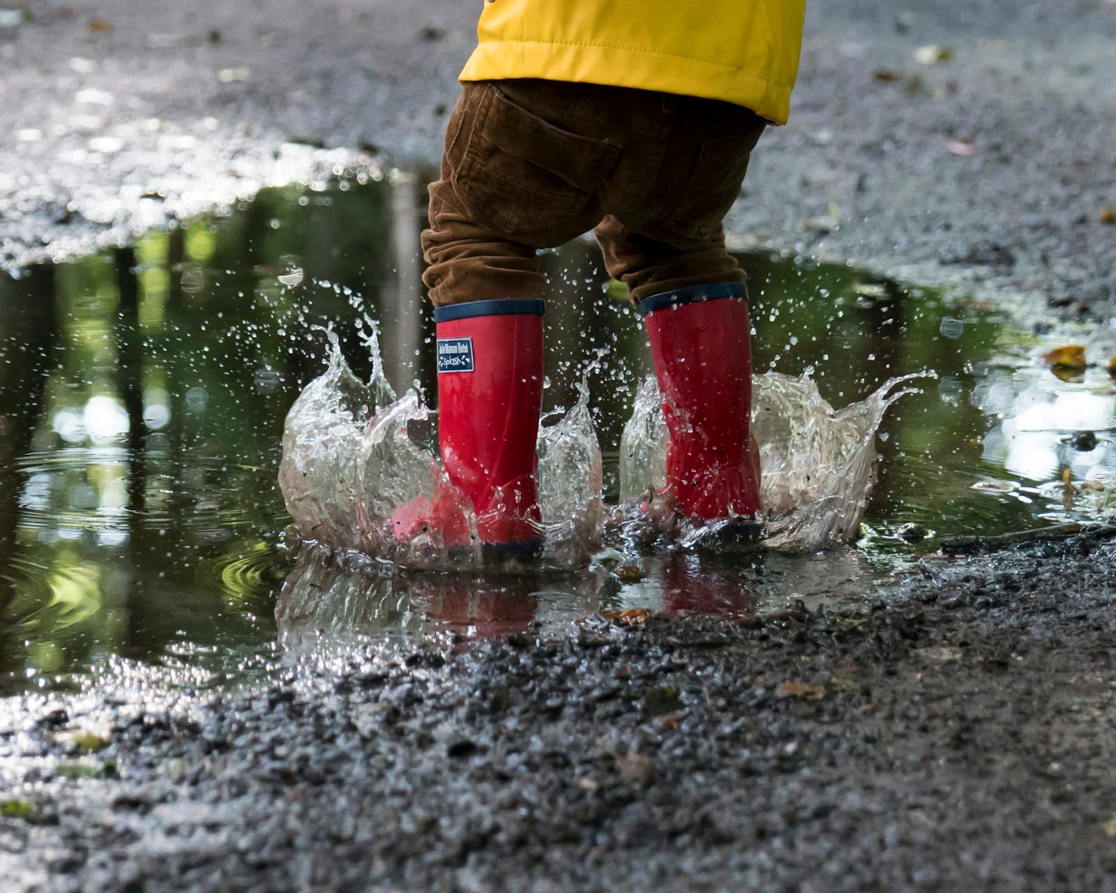 A child in red wellies splashing through a puddle on a woodland path